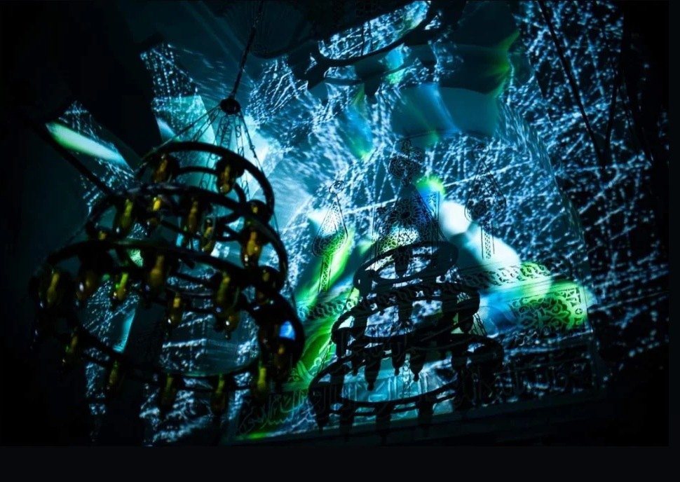 Chandeliers silhouetted against cyan and green star data projected on the vaults
