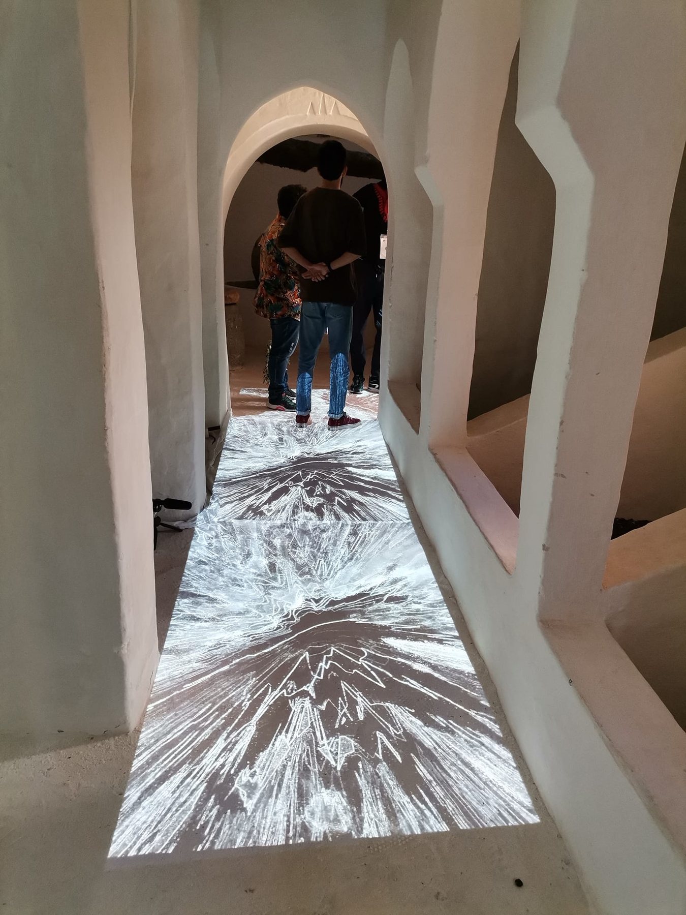 Generative projection running along the floor of a narrow arched passage, with visitors at the far end